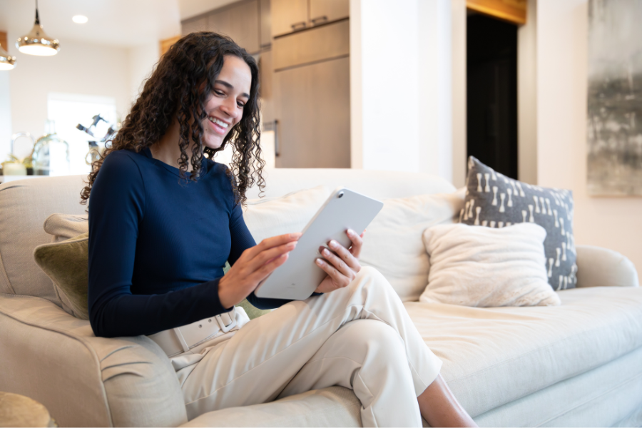 Woman relaxing on a couch using a tablet in a bright, modern living room, highlighting comfortable everyday use of smart home technology and connected living.