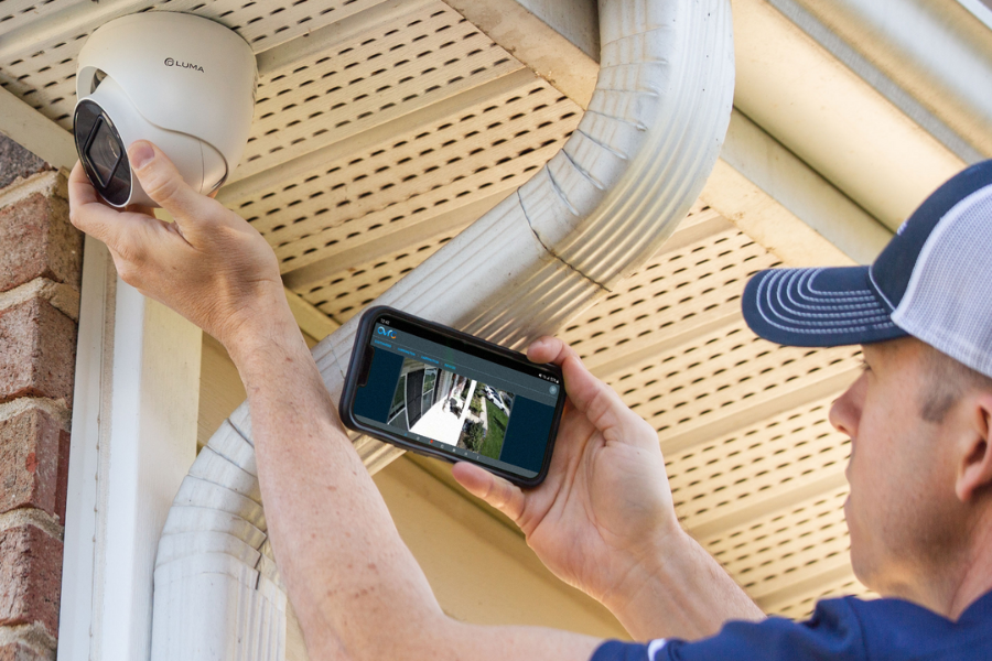 Technician installing an outdoor security camera while viewing the live feed on a smartphone, highlighting real-time monitoring and professional surveillance system setup.