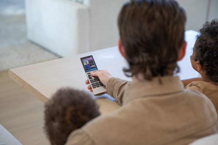 Person using a handheld remote to control a smart home system while sitting with family, highlighting simple, shared control of home entertainment and automation features.