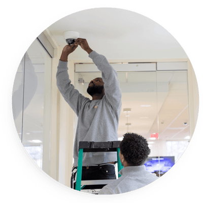 Technician installing a ceiling-mounted security camera indoors while another person observes, highlighting professional surveillance setup for interior monitoring and safety.