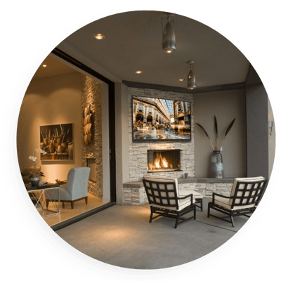 Outdoor living space with patio seating, fireplace, and a mounted TV displaying scenic content, highlighting integrated outdoor entertainment with audio-visual comfort and modern smart home design.