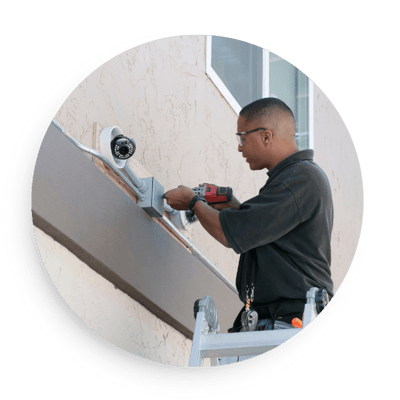 Technician installing an outdoor security camera on a home exterior using tools and ladder, highlighting professional surveillance system setup for reliable home security.